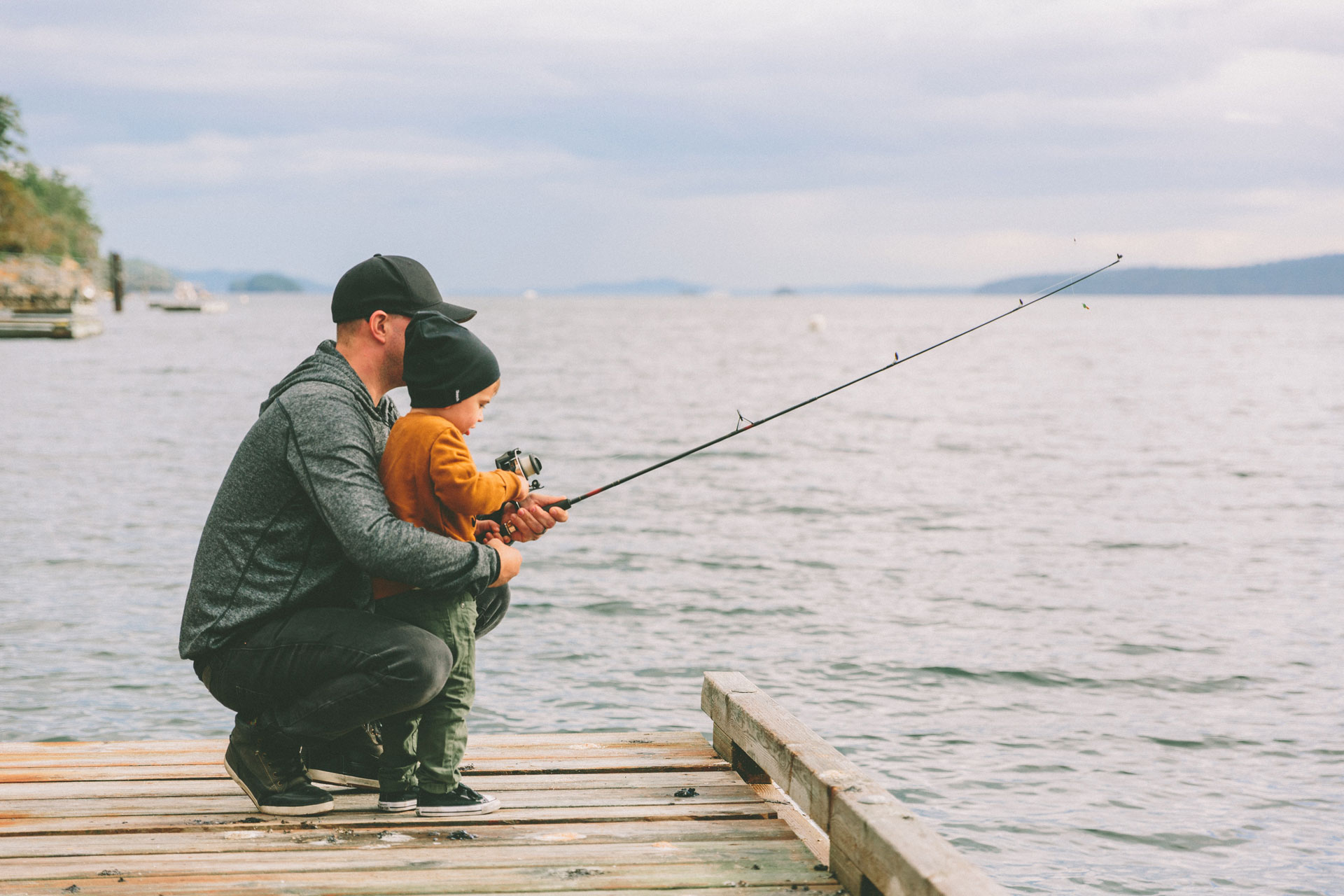 father fishing with son on a deck of a lake